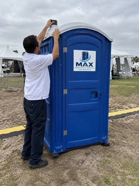 Max Porta Potty Rentals technician restocking a portable restroom unit on site
